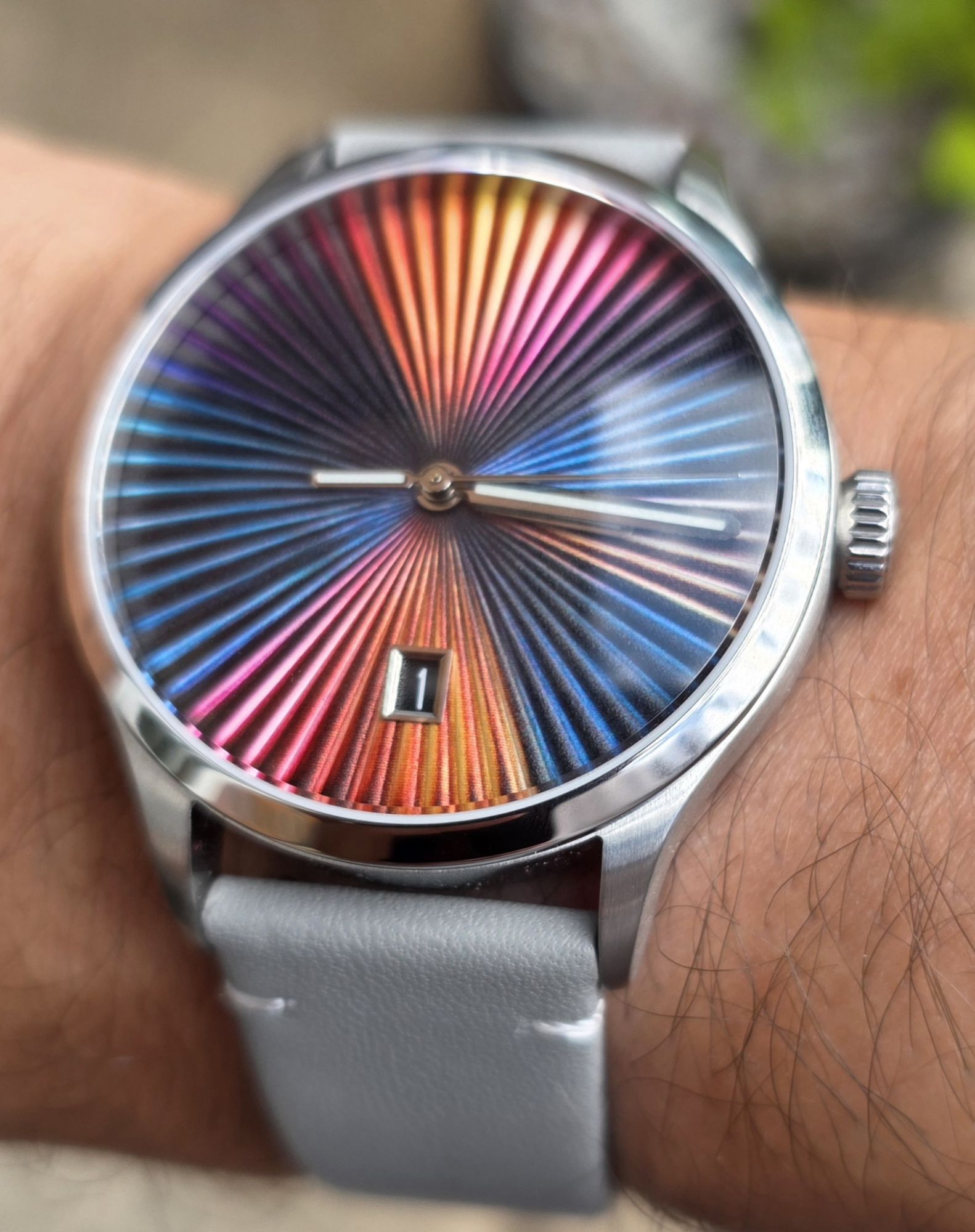 Review: Mezei First Anniversary Edition Close-up wrist shot of the Mezei First Anniversary Edition watch fitted on a light grey leather strap, showcasing its vibrant rainbow sunburst textured dial and date display.