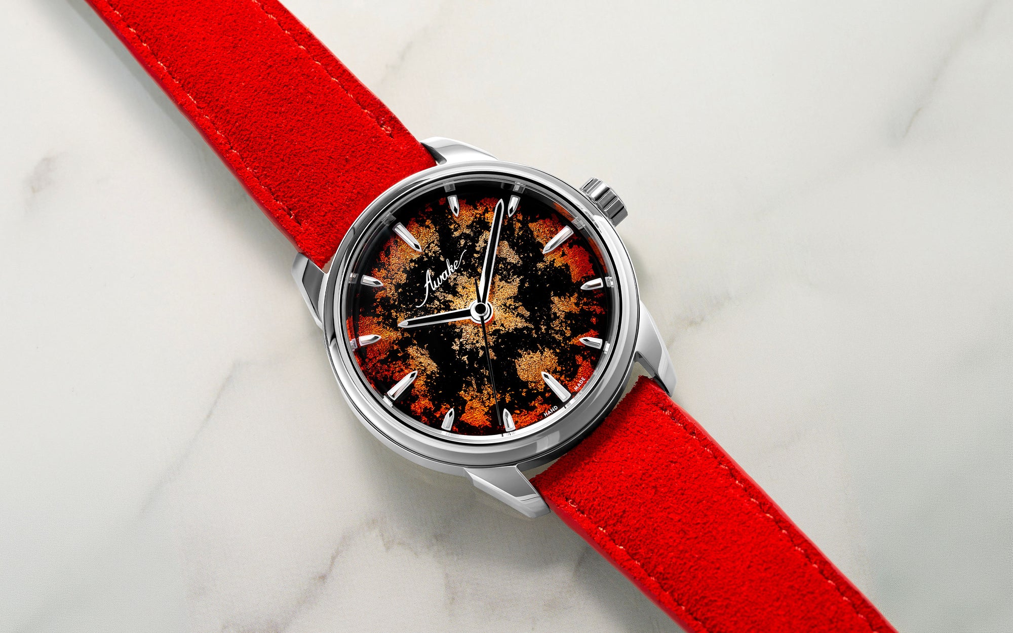 Awake Watches Overhead shot of an Awake Son Mai artisanal watch featuring a red, black, and gold foil lacquered dial paired with a vibrant red suede strap on a white marble background.