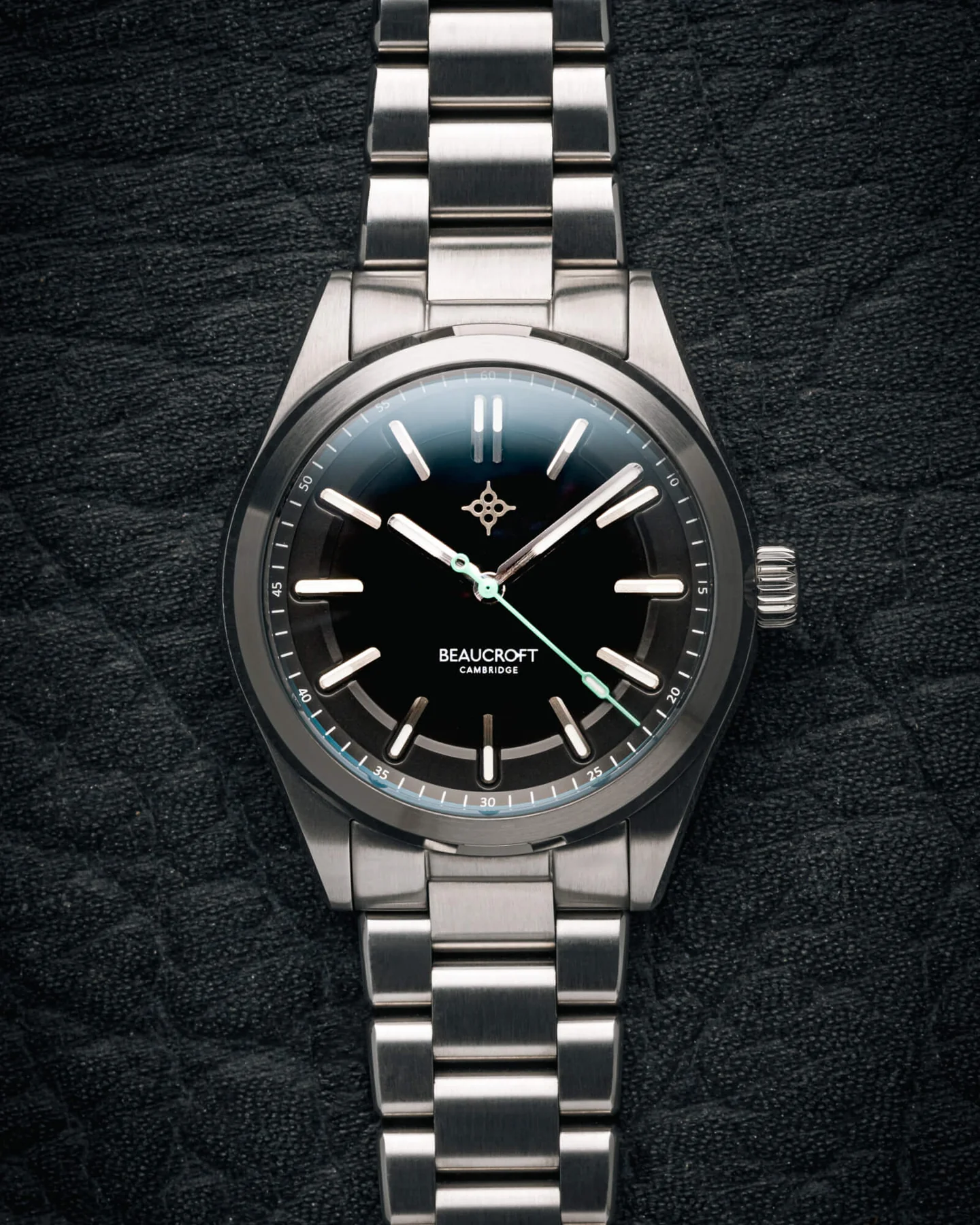 Beaucroft Front-facing view of a Beaucroft Cambridge Element Obsidian watch with a deep black dial, polished indices, mint green seconds hand accent, and stainless steel integrated bracelet set against a textured dark background.