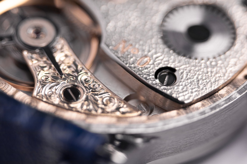 Extreme macro close-up of a luxury watch movement showing hand-engraved scrollwork, polished screws, and textured metal finish.