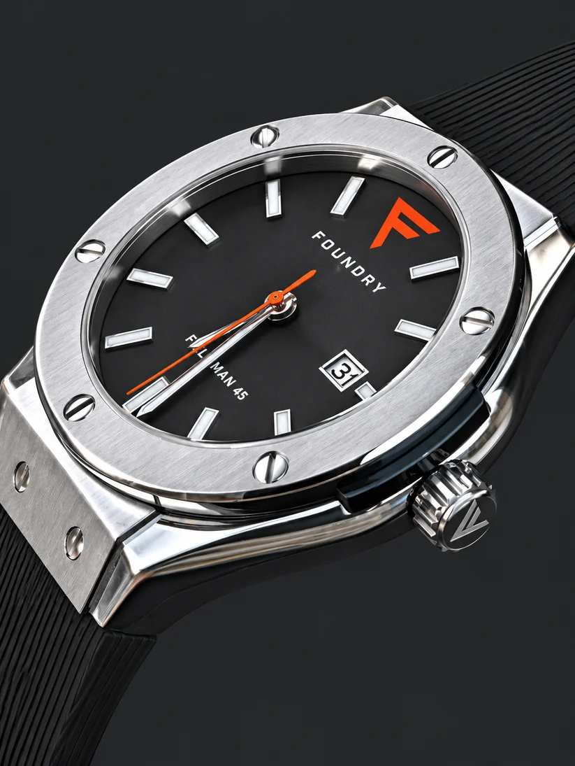 Foundry Watch Co. Close-up shot of the Foundry Foreman 45 watch featuring a brushed steel bezel with exposed screws, a black dial with an orange logo and orange seconds hand, and a black silicone strap.