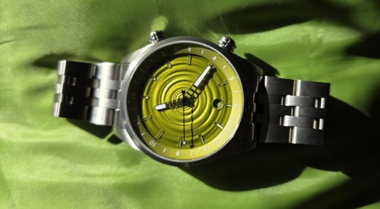 Direct overhead shot of The Skipping Stone by Golby watch on a green fabric backdrop, highlighting the water-ripple pattern on the lime-green dial.
