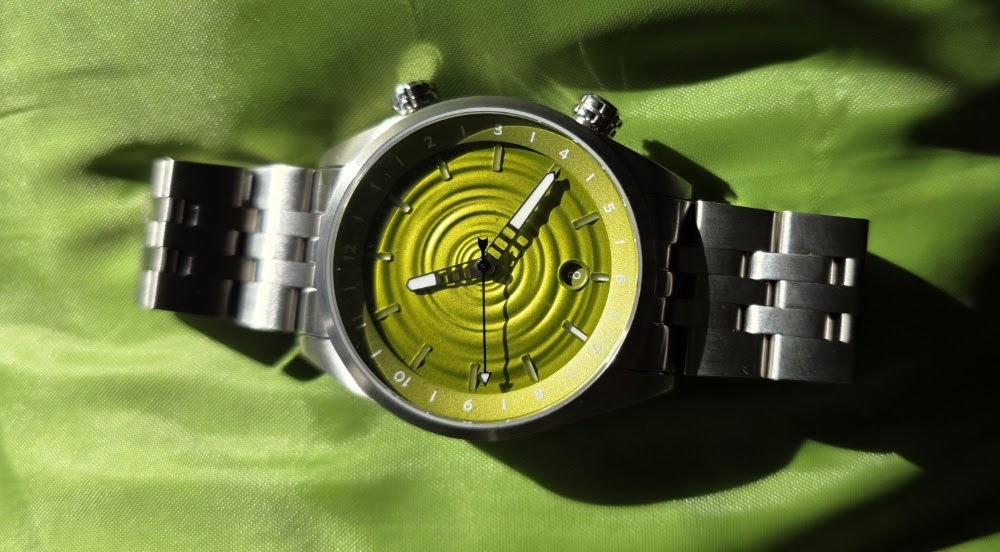 Direct overhead shot of The Skipping Stone by Golby watch on a green fabric backdrop, highlighting the water-ripple pattern on the lime-green dial.