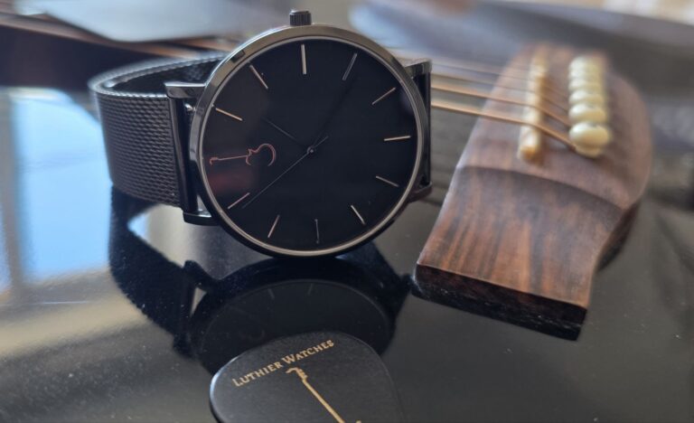 LP Black watch with mesh bracelet displayed on an acoustic guitar body alongside a branded guitar pick.