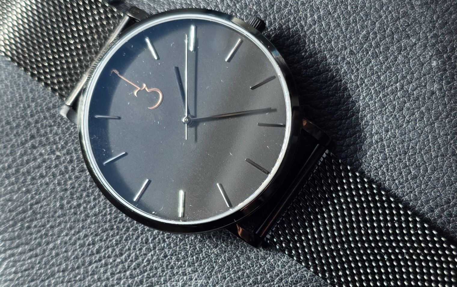 Review: Luthier LP Close-up of the Luthier LP Black watch dial showing the rose gold guitar cutaway logo at 12 o'clock and black mesh bracelet.