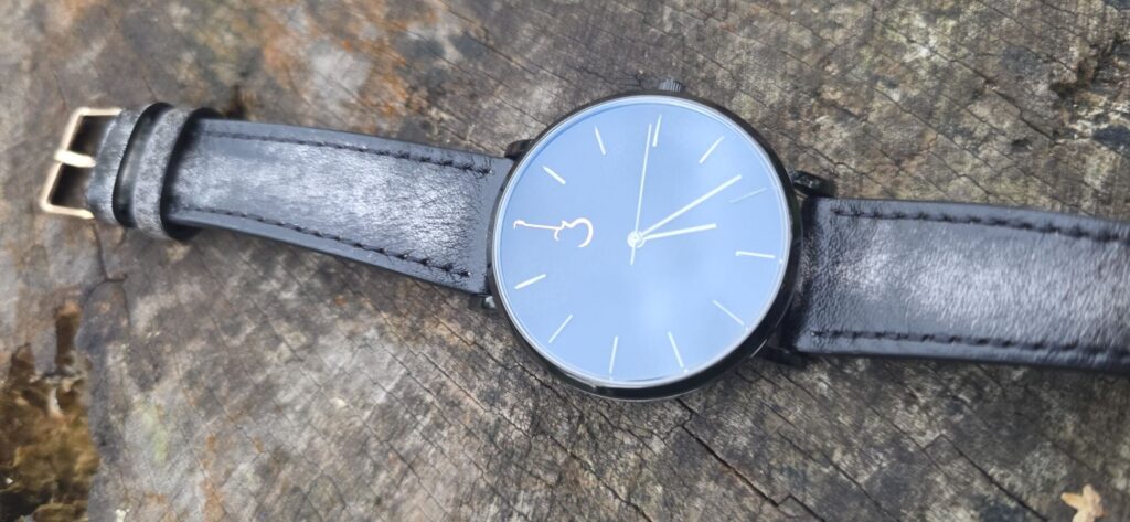 Luthier Luthier LP Black watch paired with a distressed grey-black leather strap on a wooden surface.