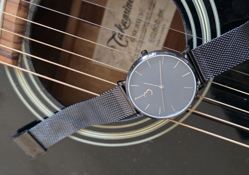 Luthier Luthier LP Black watch resting on the strings over the soundhole of an acoustic guitar.