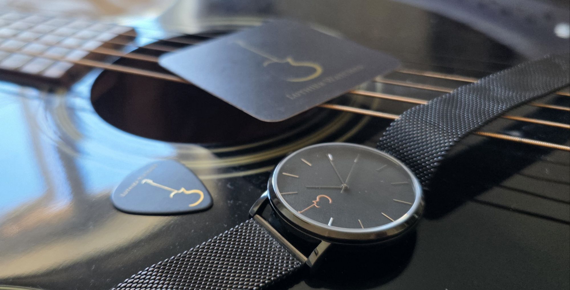 Review: Luthier LP Luthier LP Black watch displayed with branded plectrum and guarantee card on an acoustic guitar body.