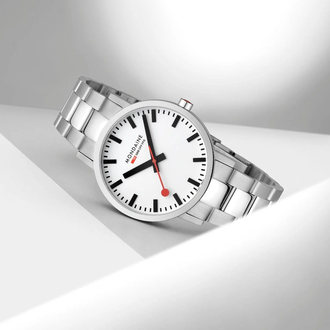 Angled studio shot of the iconic Mondaine classic Swiss railway watch featuring a clean white dial, black hour markers, distinctive red lollipop second hand, and stainless steel bracelet.