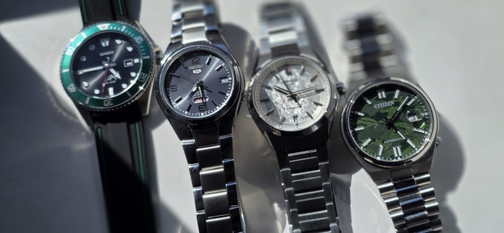 Lineup of four men's stainless steel wristwatches including a green Casio diver, Seiko 5, silver dial model, and green camo pattern Citizen watch
