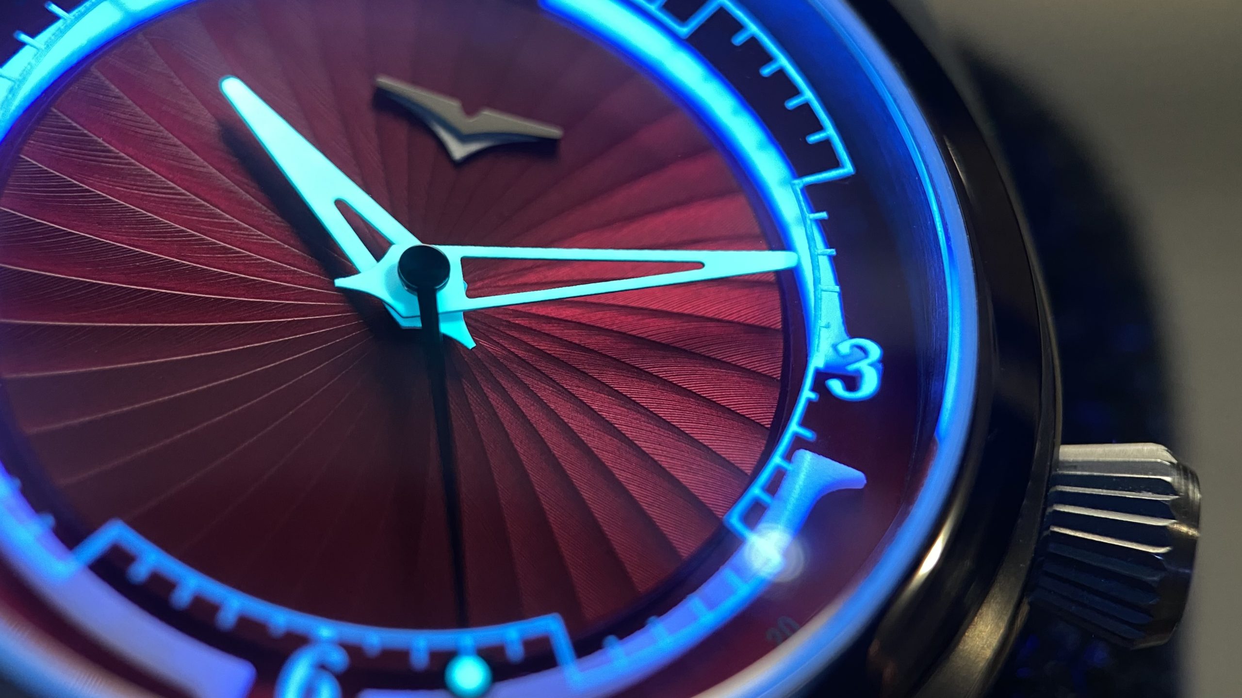 Valour Watches Close-up macro lume shot of a Valour watch featuring a vibrant red sunburst dial, glowing blue Super-LumiNova chapter ring and hands, and a polished stainless steel case.